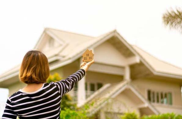 Photo of a woman holding up a block house in front of real house